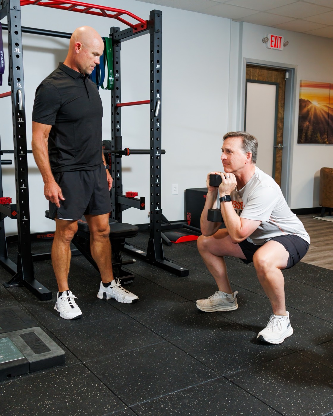 A FINISH coach guiding a goblet squat on the performance floor