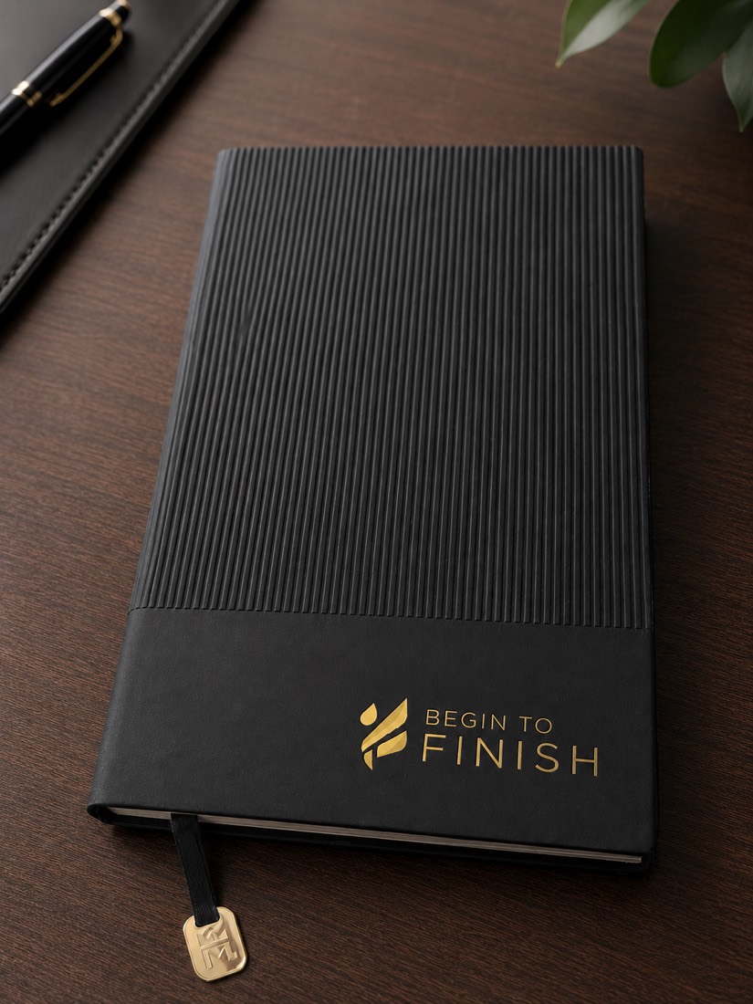 The Begin to FINISH journal at an angle, showing its ribbed spine and gold foil logo